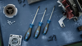 Three hex screwdrivers on a metal workbench beside bolts and machine parts.