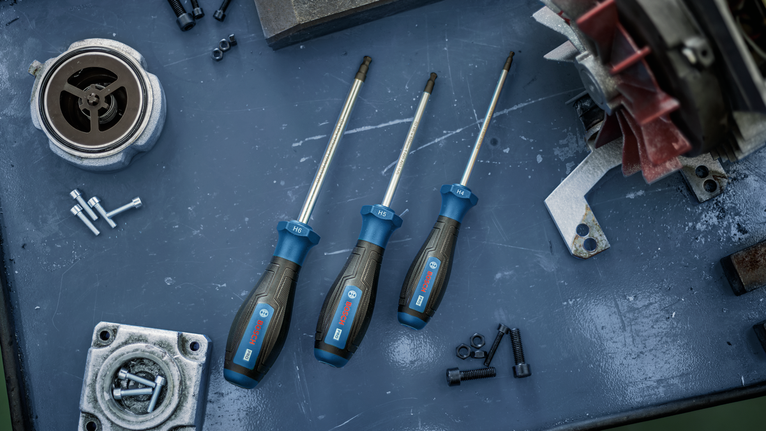 Three hex screwdrivers on a metal workbench beside bolts and machine parts.