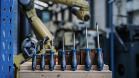 A set of blue-handled screwdrivers is arranged on a workbench in a factory.