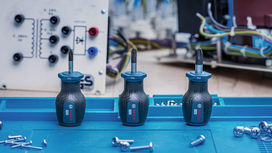 Three screwdrivers stand on a blue tray surrounded by screws and electronic components.