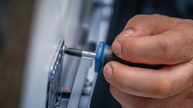 Person using a screwdriver to tighten a screw on a metal plate.