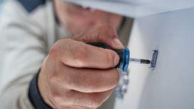 Person using a screwdriver to fasten a screw into a wall.