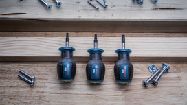 Three screwdrivers arranged on wood next to scattered screws and bolts.