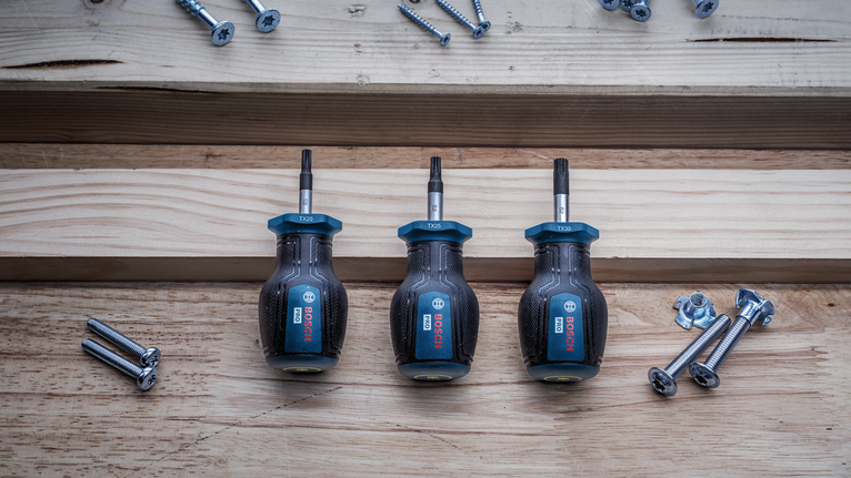 Three screwdrivers arranged on wood next to scattered screws and bolts.