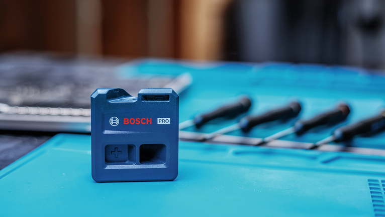 Blue tool accessory is placed on a blue work surface with screwdrivers in the background.