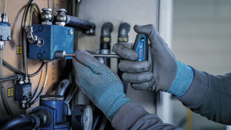 Person wearing safety equipment tightens a bolt on industrial machinery.