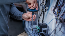 Person tightens a bolt inside an electrical panel using a T-handle wrench.