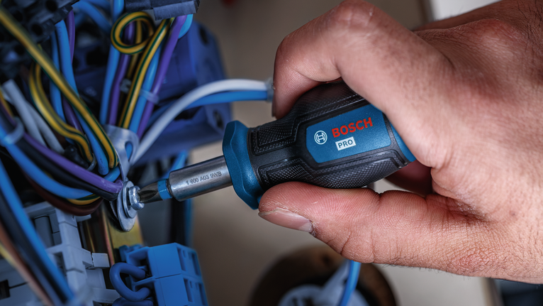 Person tightens a screw among electrical wires using a screwdriver.