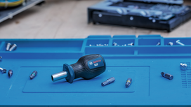 Manual screwdriver and assorted bits placed on a blue work surface.