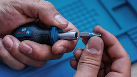 Person holding a screwdriver and inserting a bit on a blue work surface.
