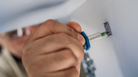 Person wearing safety equipment secures a metal bracket to a wall with a screwdriver.