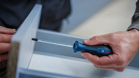 Person uses a screwdriver to fasten a screw into a piece of furniture.