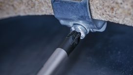 Screwdriver bit tightening a screw into a metal bracket attached to stone.