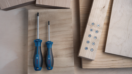 Two screwdrivers on a wooden surface beside planks joined with screws.