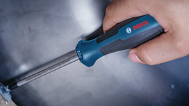 Person using a screwdriver to tighten a screw on a metal surface.
