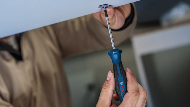 Person fastens a screw into the ceiling using a blue and black screwdriver.