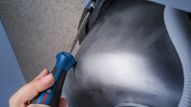 Person tightens a screw under a metal sink using a screwdriver.