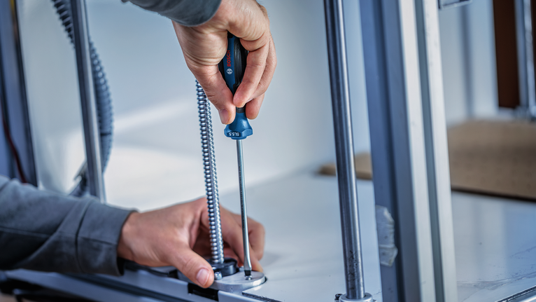 Person using a screwdriver to fasten a metal conduit inside a cabinet.