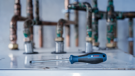 Flathead screwdriver resting on a metal surface in front of industrial pipes.