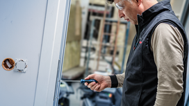 Person wearing safety equipment tightens a door hinge with a screwdriver.