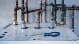 Flathead screwdriver lies on top of a boiler near several rusted pipes.
