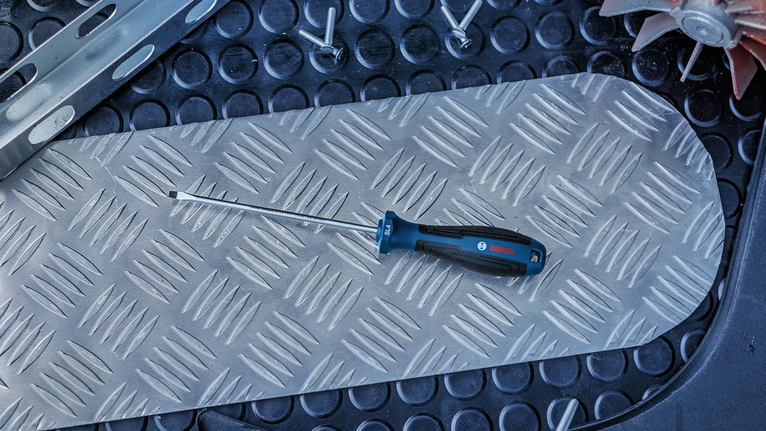 Flathead screwdriver resting on a textured metal plate.