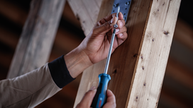 Person uses a screwdriver to drive a screw into a wooden beam.