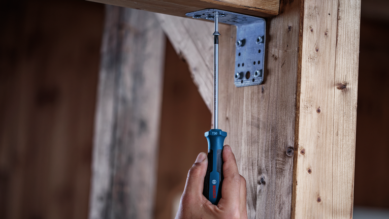 Person tightens a screw into a metal bracket on a wooden frame.