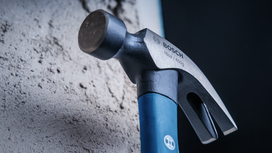 Steel claw hammer with a blue handle resting against a concrete wall.