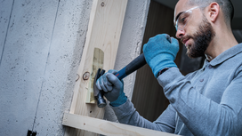 Person wearing safety equipment uses a hammer to work on a wooden board.