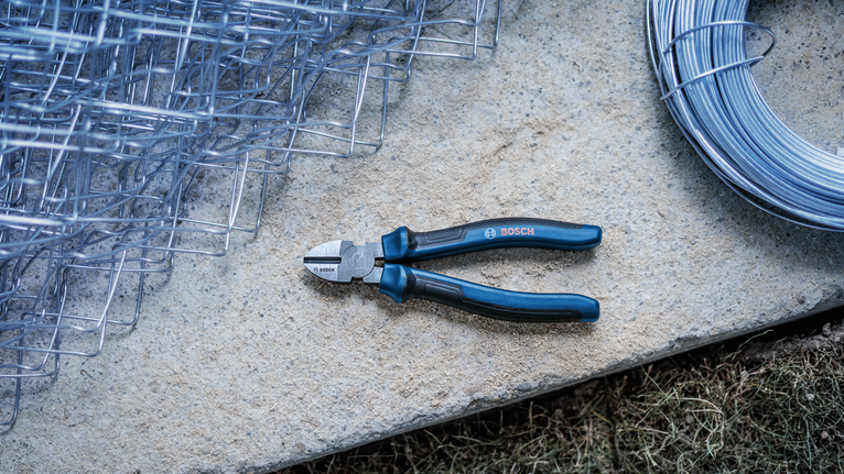 Wire cutter with blue handles lying on a stone slab next to metal fencing and rolled wire.