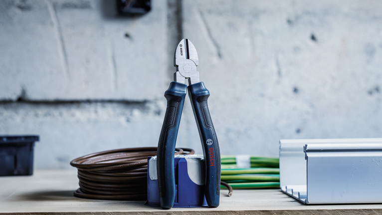Wire cutter standing upright on a workbench next to coiled cables and a metal channel.
