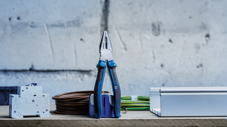 Pliers standing upright on a workbench beside electrical components and coiled cables.