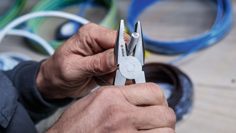 Person uses pliers to strip insulation from electrical wire.