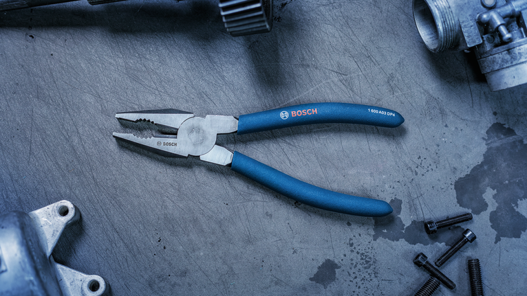 Blue-handled pliers lying on a metal work surface beside metal bolts and parts.