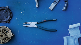 Combination pliers placed on a blue workbench surrounded by metal and plastic parts.