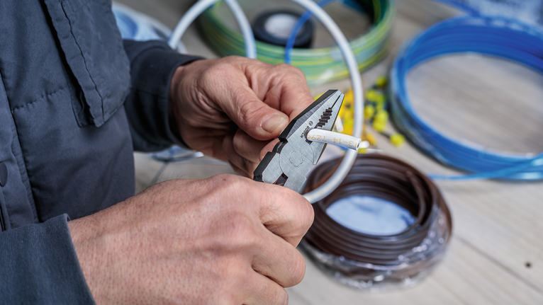 Person strips the insulation from an electrical wire using pliers.