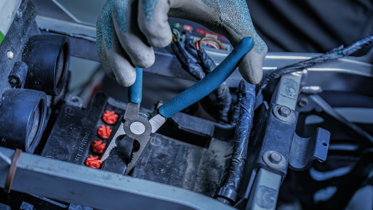 Person wearing safety equipment cuts wire in an engine compartment.