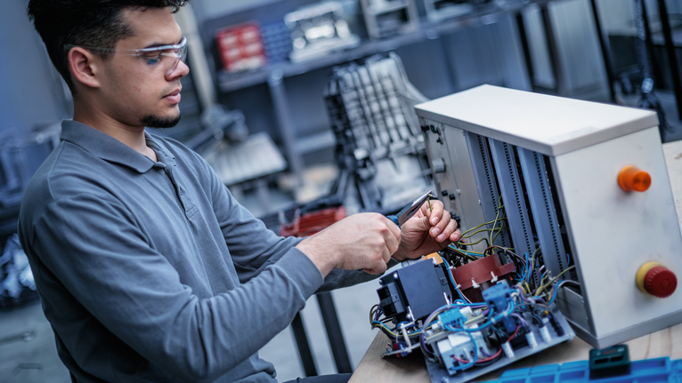Person wearing safety equipment repairs wiring inside an industrial control panel.