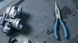 Long-nose pliers and a mechanical component on a metal surface.