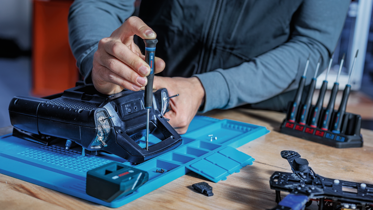 Person assembles a device on a blue workstation using a screwdriver.