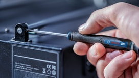 Person using a screwdriver to tighten a small screw on electronic equipment.