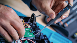 Person using a screwdriver to work on electronic components.