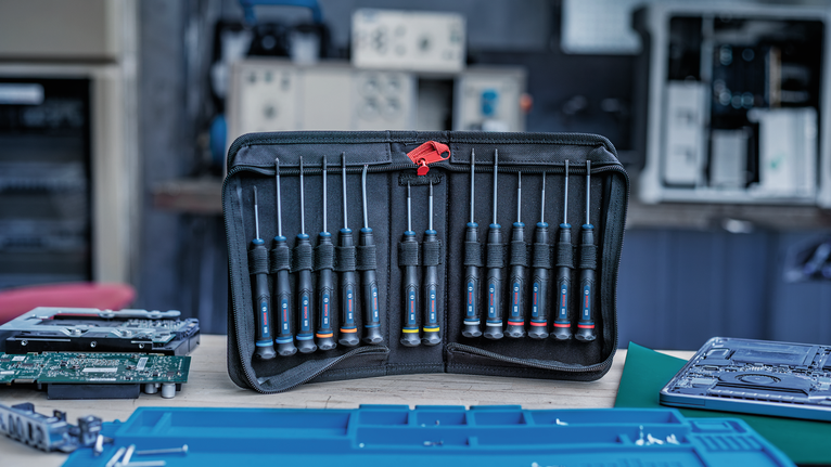 Set of precision screwdrivers arranged in a black tool pouch on a workbench.