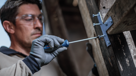 Person wearing safety equipment tightens screws on a wood beam with a screwdriver.