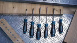 Six screwdrivers with black and blue handles arranged on a metal checker plate surface.