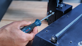 Person using a screwdriver to tighten a screw on a black metal device.