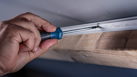Person uses a screwdriver to fasten a screw into a metal rail attached to wood.