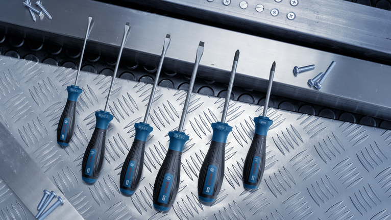 A set of screwdrivers arranged on a metal surface next to scattered screws.