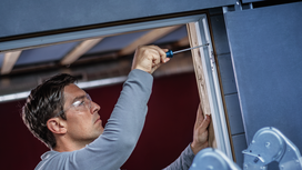 Person wearing safety equipment fastens a screw into a door frame with a screwdriver.
